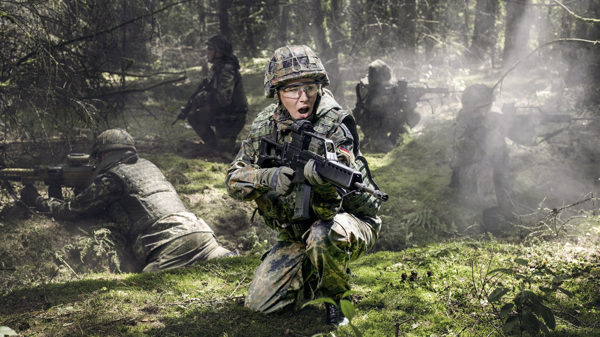 Ein Soldatin mit Gewehr sichert mit Kameraden ein Waldstück